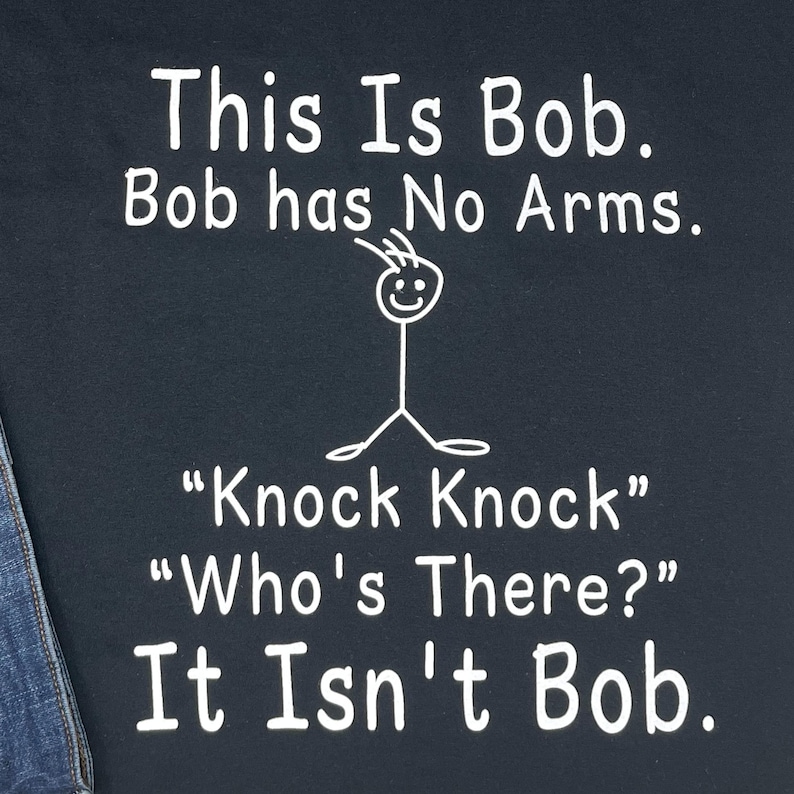 Pu&ograve; includere: T-shirt blu navy con testo bianco: "This Is Bob. Bob has No Arms." Un pupazzetto stilizzato senza braccia &egrave; disegnato sopra il testo. Sotto c'&egrave; "Knock Knock" "Who's There?" It Isn't Bob."