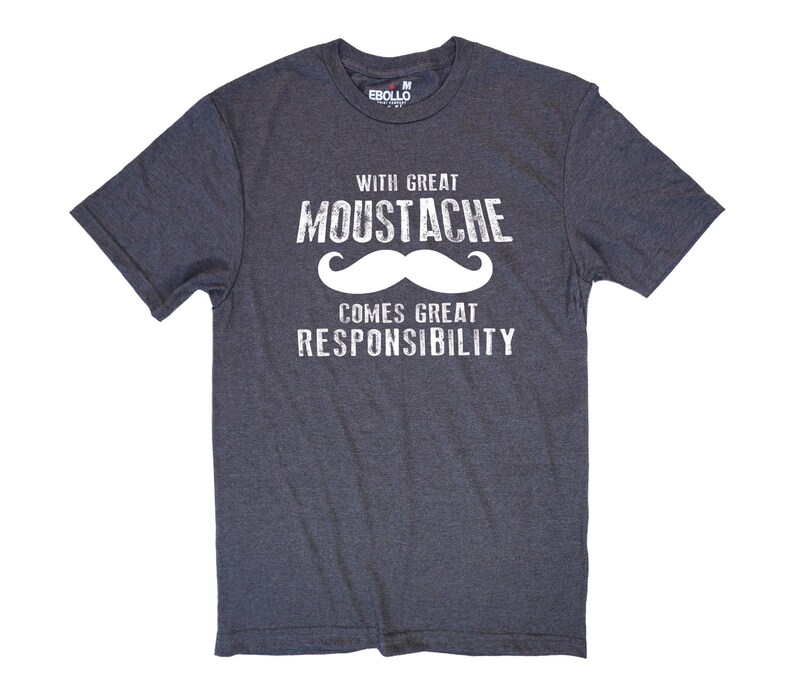 May include: Dark gray t-shirt with the text "WITH GREAT MOUSTACHE COMES GREAT RESPONSIBILITY" in white. The word "MOUSTACHE" features a white mustache graphic. The shirt is short-sleeved and has a crew neck.