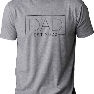 May include: Gray t-shirt with a black outline of the word "DAD" in a box with the text "EST. 2022" underneath.