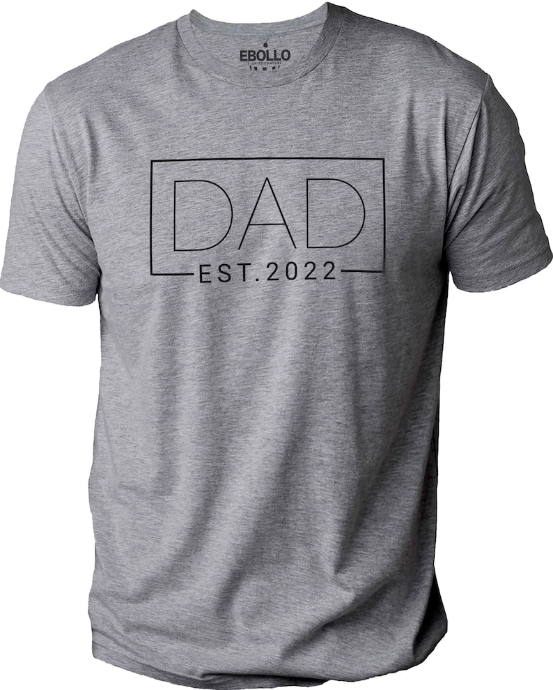 May include: Gray t-shirt with a black outline of the word "DAD" in a box with the text "EST. 2022" underneath.