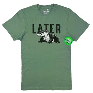 Op de afbeelding: Een groen T-shirt met een zwarte alligator-print en het woord "LATER" in het zwart gedrukt. Het shirt is maat M voor heren.