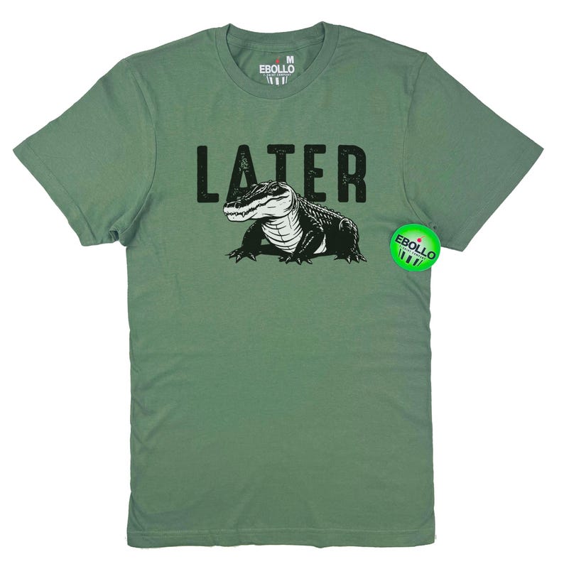 Op de afbeelding: Een groen T-shirt met een zwarte alligator-print en het woord "LATER" in het zwart gedrukt. Het shirt is maat M voor heren.
