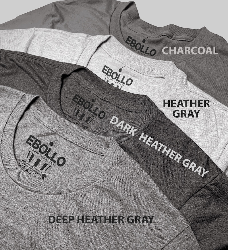 May include: Four t-shirts in different shades of gray, from light to dark. The t-shirts are stacked on top of each other, with the darkest gray t-shirt on the bottom. Each t-shirt has a label with the text "EBOLLO T-SHIRT COMPANY" and the color of the t-shirt. The colors are: Deep Heather Gray, Dark Heather Gray, Heather Gray, and Charcoal.