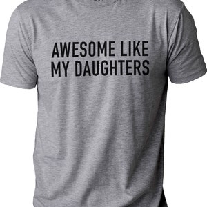 May include: A grey t-shirt featuring the black text "AWESOME LIKE MY DAUGHTERS". The shirt has a crew neck and short sleeves. The brand name "EBOLLO" is printed on the upper back of the shirt.