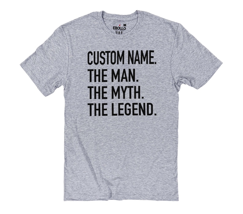 Op de afbeelding: Een lichtgrijs t-shirt met de tekst "CUSTOM NAME. THE MAN. THE MYTH. THE LEGEND." in vette zwarte letters. Het shirt heeft korte mouwen en een ronde hals.
