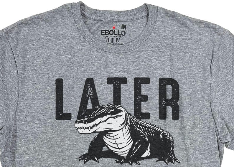 Op de afbeelding: Grijs T-shirt met een zwarte alligator-afbeelding en het woord "LATER" in het zwart gedrukt.