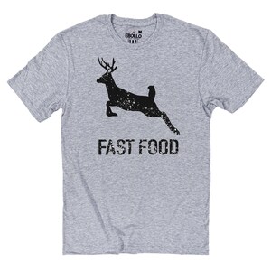 May include: A grey t-shirt with a black deer silhouette leaping, speckled with white dots. The words "FAST FOOD" are printed below in a distressed font. The shirt has a crew neck and short sleeves.