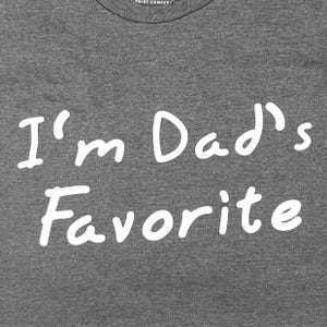 Peut inclure: T-shirt gris avec un texte blanc qui dit "Je suis le pr&eacute;f&eacute;r&eacute; de papa"