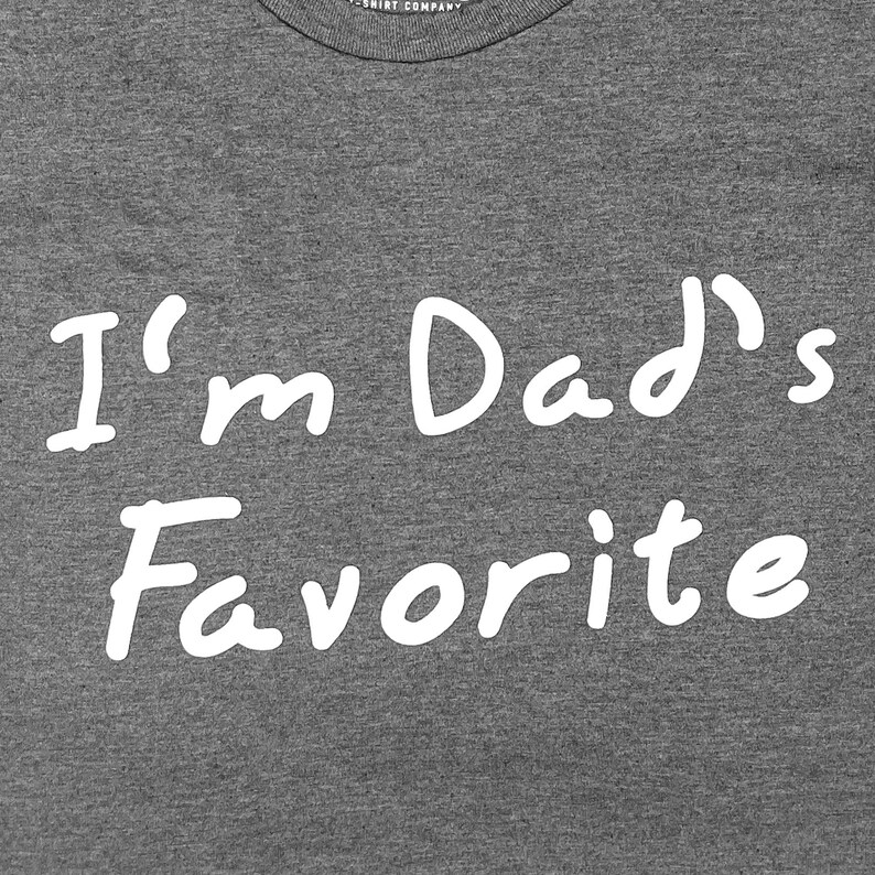 Peut inclure: T-shirt gris avec un texte blanc qui dit "Je suis le pr&eacute;f&eacute;r&eacute; de papa"