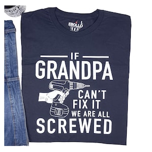 Puede incluir: Camiseta azul marino con el texto blanco "IF GRANDPA CAN'T FIX IT WE ARE ALL SCREWED" y un dibujo de un taladro. La camiseta se muestra junto a un peto vaquero.