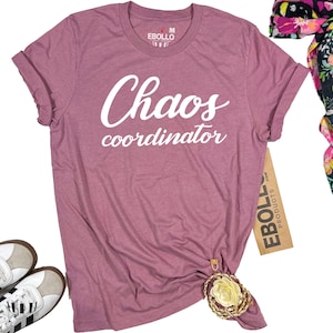 May include: A mauve colored t-shirt with the text "Chaos coordinator" printed in white on the front.