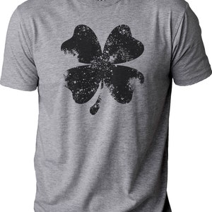 May include: A heather gray t-shirt featuring a distressed black four-leaf clover graphic. The shirt has a crew neck and short sleeves. The brand name "EBOLLO" is printed on the collar.