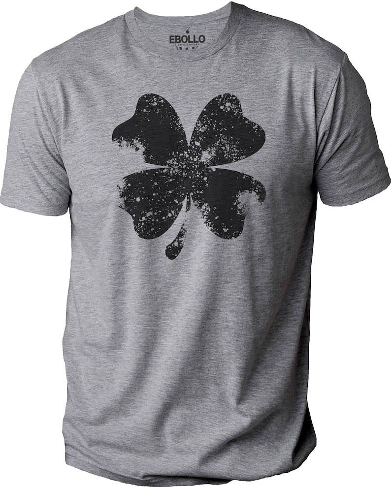May include: A heather gray t-shirt featuring a distressed black four-leaf clover graphic. The shirt has a crew neck and short sleeves. The brand name "EBOLLO" is printed on the collar.