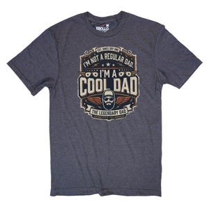 May include: Dark gray t-shirt with a graphic that reads "I'M NOT A REGULAR DAD. I'M A COOL DAD" in a vintage style. The graphic features a bearded man wearing sunglasses and a baseball cap, with wings and stars.