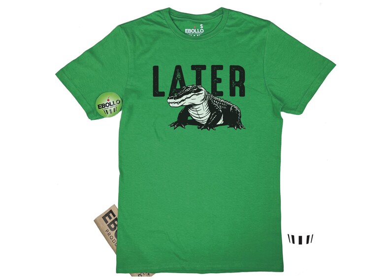 Op de afbeelding: Groen T-shirt met een zwarte alligator-afbeelding en het woord "LATER" in witte tekst.