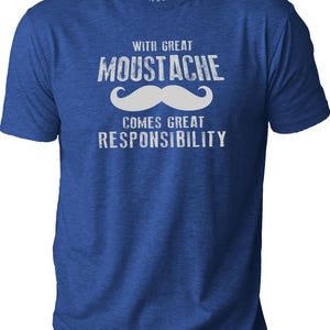 May include: Blue t-shirt with the text "WITH GREAT MOUSTACHE COMES GREAT RESPONSIBILITY" in white. The word "MOUSTACHE" is above a white mustache graphic. The shirt has short sleeves and a crew neck.