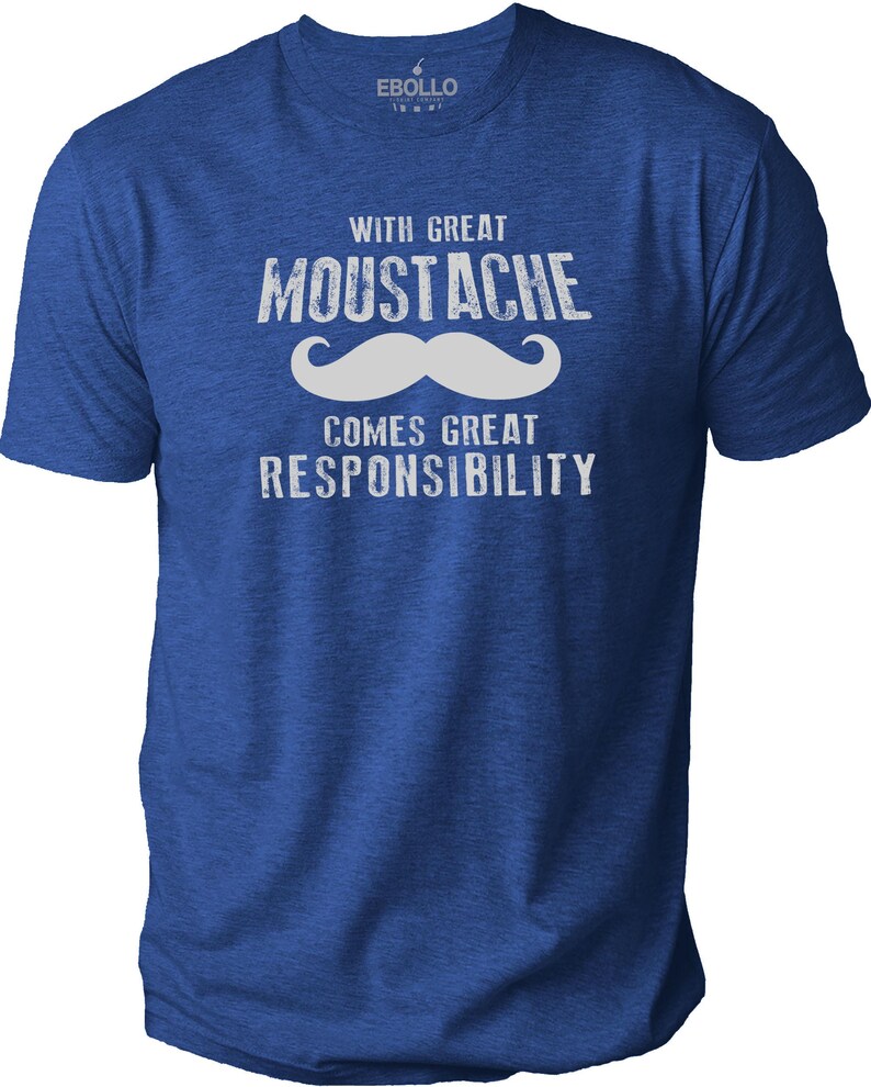 May include: Blue t-shirt with the text "WITH GREAT MOUSTACHE COMES GREAT RESPONSIBILITY" in white. The word "MOUSTACHE" is above a white mustache graphic. The shirt has short sleeves and a crew neck.