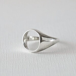 Op de afbeelding: Een gepolijste zilveren ring met een holle ovale midden. De ring heeft een gladde, afgeronde band en een plat, ovaal vlak. De ring staat tegen een witte achtergrond, wat het reflecterende oppervlak benadrukt. Een minimalistisch ontwerp, geschikt voor dagelijks gebruik.
