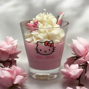 Pode incluir: Uma vela rosa com tema Hello Kitty em um pote de vidro com cobertura de chantilly branco e um canudo listrado vermelho e branco.