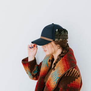 Könnte beinhalten: Eine Frau trägt eine marineblaue Baseballkappe mit Ohrenschützern und eine Jacke mit braunem, rotem und türkisfarbenem Muster.