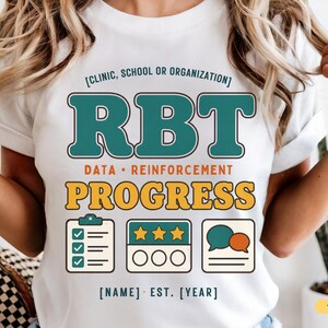 Könnte beinhalten: Ein weißes T-Shirt mit einem Aufdruck, der den Text [CLINIC, SCHOOL OR ORGANIZATION], RBT, DATA • REINFORCEMENT, PROGRESS sowie [NAME] • EST. [YEAR] enthält. Das Design zeigt Symbole einer Checkliste, drei Sterne und zwei Sprechblasen in Blaugrün und Gold.