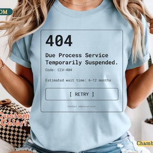 May include: Light blue t-shirt with a graphic displaying a 404 error message: "Due Process Service Temporarily Suspended." The text includes a code, wait time, and a "Retry" button. The shirt is labeled "Chambray."