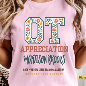 Puede incluir: Una camiseta rosa claro con las letras OT en un patrón floral, seguidas del texto APPRECIATION, MADISON BROOKS, COTA • WILLOW CREEK LEARNING ACADEMY y OCCUPATIONAL THERAPY impreso en varios colores y fuentes en la parte frontal de la prenda.