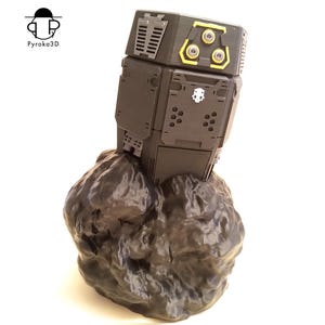 Op de afbeelding: Een zwarte en grijze robot met gele accenten en meerdere sensoren bovenop, staande op een grijze rotsachtige basis.