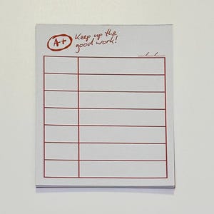 May include: A white notepad with a red border and lines for writing. The top left corner has a red circle with "A+" inside. Above the lines, the text reads "Keep up the good work!"