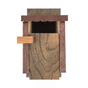 Puede incluir: Una pequeña caja de madera con una tapa con bisagras y un pequeño pestillo de madera. La caja está hecha de madera marrón oscura con un borde de madera marrón claro. La caja está cerrada.