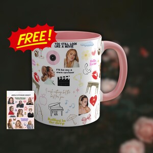 Puede incluir: Una taza de cerámica rosa y blanca con un diseño que presenta un collage de imágenes y texto, incluyendo "You still look like a movie", "I'll be my own saviour", "Rolling in the deep", y "Hello, it's me". La taza viene con una hoja de pegatinas con imágenes de Adele.