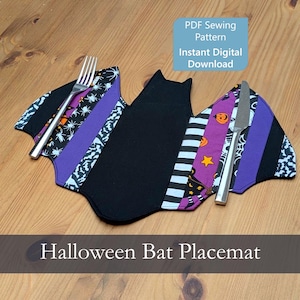 May include: A bat-shaped fabric placemat featuring a central black panel flanked by striped, purple, and patterned fabric sections with spider, pumpkin, and star motifs. A silver fork and knife rest on the wings. Text reads PDF Sewing Pattern.
