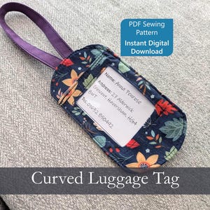 May include: A navy blue luggage tag with a floral pattern, featuring orange and yellow flowers and green leaves. It has a clear window for an address card and a purple handle. Text on the tag reads "Curved Luggage Tag".