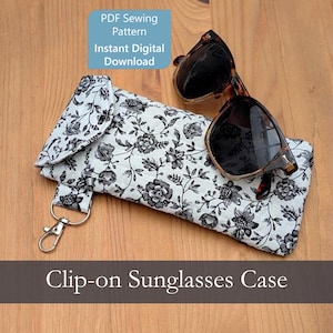 May include: A quilted fabric sunglasses case featuring a black and white floral pattern, a fold-over flap, and a silver-toned metal lobster clasp. The case is displayed with a pair of brown tortoiseshell sunglasses and text reading PDF Sewing Pattern.