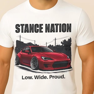 May include: White t-shirt featuring a red sports car graphic with the text "STANCE NATION" above and "Low. Wide. Proud." below. The car is low to the ground, with a wide stance, and is set against a stylized urban backdrop.