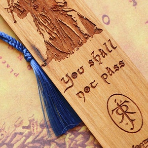 May include: Wooden bookmark with a blue tassel, featuring an engraved image of Gandalf the Grey from The Lord of the Rings. The text "You shall not pass" is engraved on the bookmark, along with the One Ring symbol.