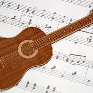 May include: A wooden acoustic guitar cutout on a sheet of music with the word "cresc." printed on the sheet music.
