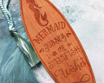 May include: Wooden surfboard bookmark with a mermaid design and the text "Mermaid Kisses and Starfish Wishes".