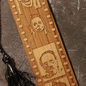 May include: Wooden bookmark with a film strip design featuring four horror movie characters. The bookmark has a black tassel.