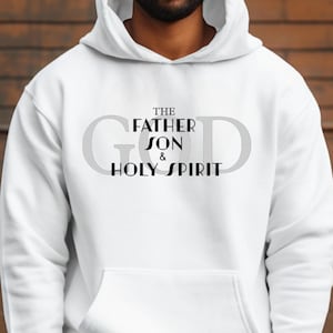 Puede incluir: Sudadera con capucha blanca con la palabra "GOD" en gris claro. Las palabras "THE FATHER SON & HOLY SPIRIT" están impresas en negro debajo. La sudadera tiene un bolsillo delantero.