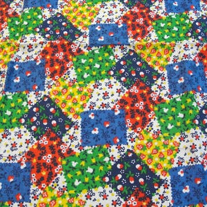 May include: A fabric featuring a patchwork pattern of square blocks in red, blue, green, and yellow. Each block contains a dense floral print with small white flowers and red strawberry motifs, creating a vibrant, repeating textile design.