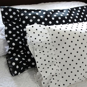 May include: Two decorative pillowcases, one black with white polka dots and the other white with black polka dots. The pillowcases are on a white bedspread. The polka dots are evenly spaced.