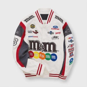 Könnte beinhalten: Eine weiße College-Jacke mit M&M-Branding, roten und grauen Ärmeleinsätzen und gestreiften Rippbündchen. Die Vorderseite zeigt gestickte Logos wie Ford, Coca-Cola und verschiedene Rennsport-Aufnäher sowie bunte M&M-Bonbon-Kreise.
