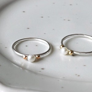 May include: Two silver rings with a single pearl and gold beads on each ring.