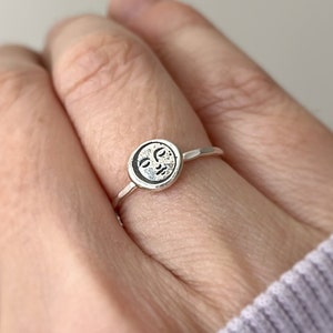 May include: A silver ring with a circular design featuring a face of the moon.