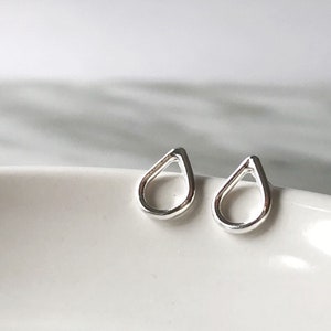 May include: A pair of silver teardrop shaped stud earrings. The earrings are simple and minimalist in design.