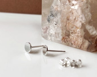 May include: A pair of silver stud earrings with round, flat fronts. The earrings are shown on a white surface.