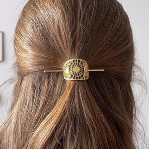 Könnte beinhalten: Goldene Haarklammer mit einem filigranen, komplizierten Design. Die Klammer ist halbkreisförmig und weist ein sich wiederholendes Muster aus kleinen Kreisen auf.