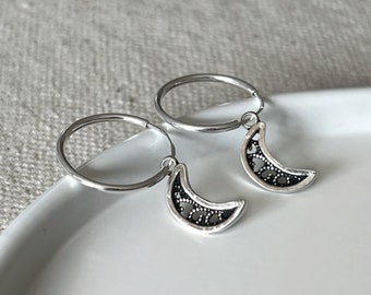 May include: A pair of silver hoop earrings with a delicate crescent moon charm hanging from each hoop.