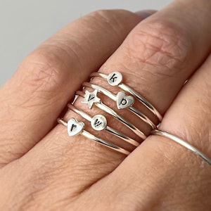 May include: A hand wearing a stack of silver rings with tiny 2mm letters, including the letters 'k', 'p', 'w', and a star. The text 'TEENY TINY 2MM LETTERS, AVAILABLE IN LOWER CASE ONLY' is at the bottom of the image. The photo makes it appear bigger, make sure to look at the measurements before you place your order.